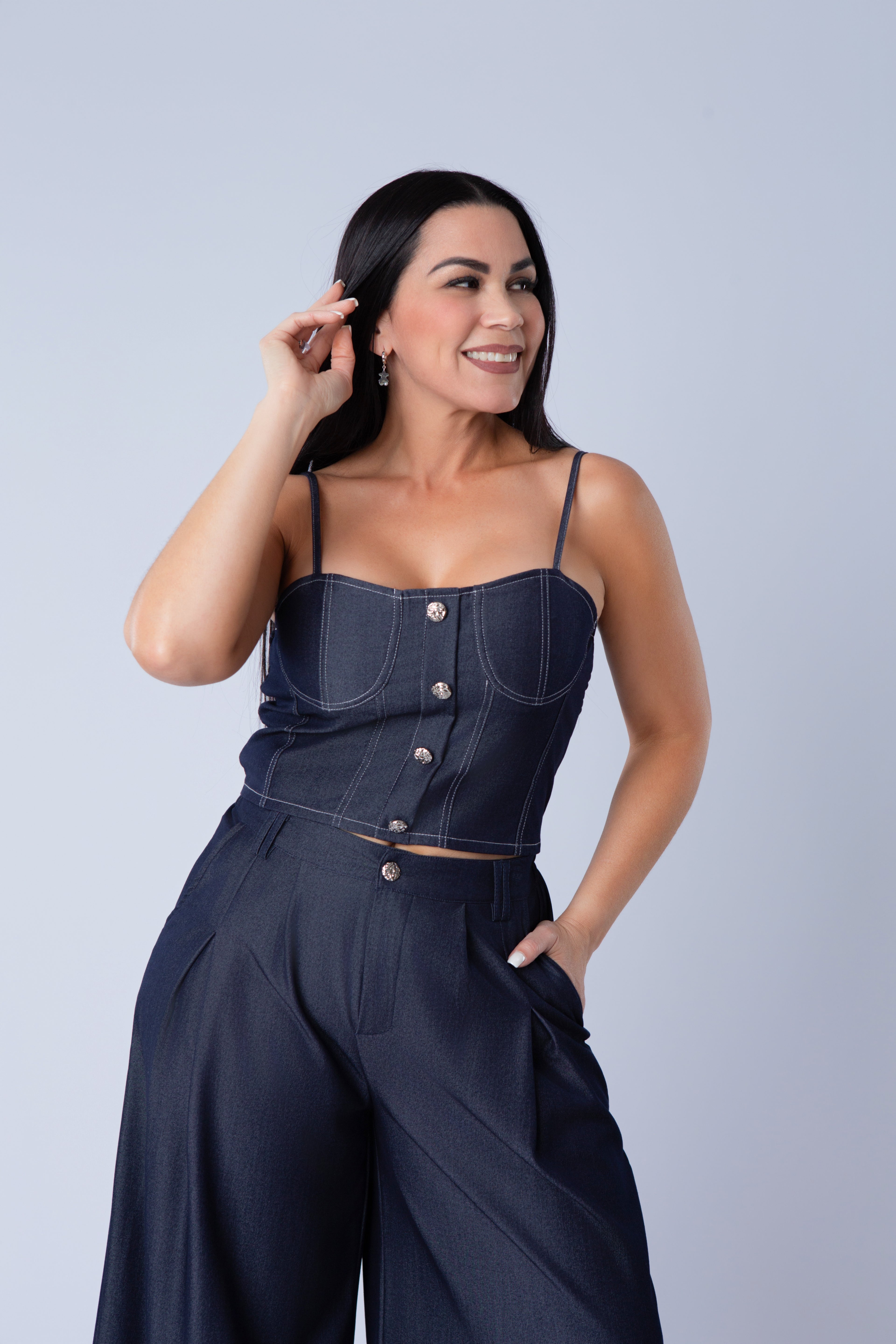 Woman wearing a navy blue denim outfit with buttons on a light gray background
